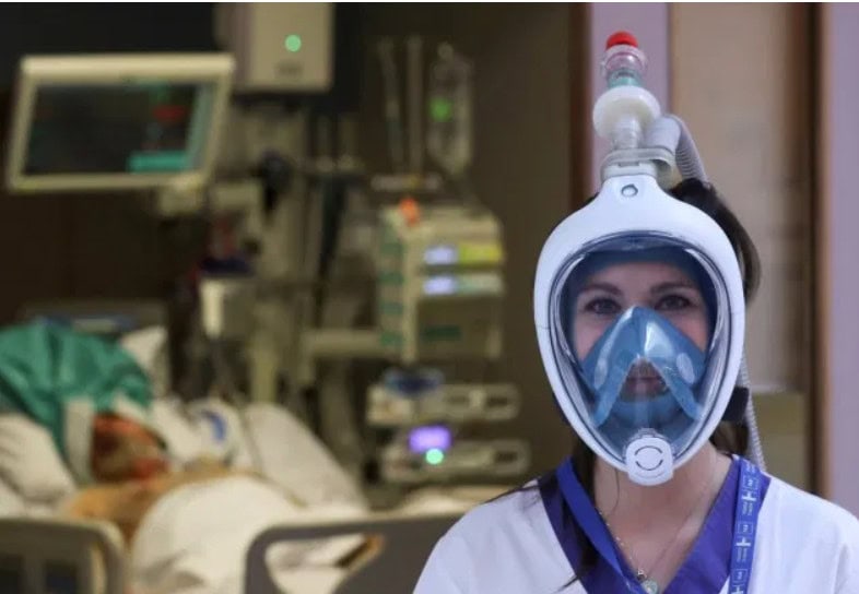 A nurse wears a full-face snorkelling mask that has been adapted by an Italian firm to make a ventilator using parts made on a 3D printer in the UK.