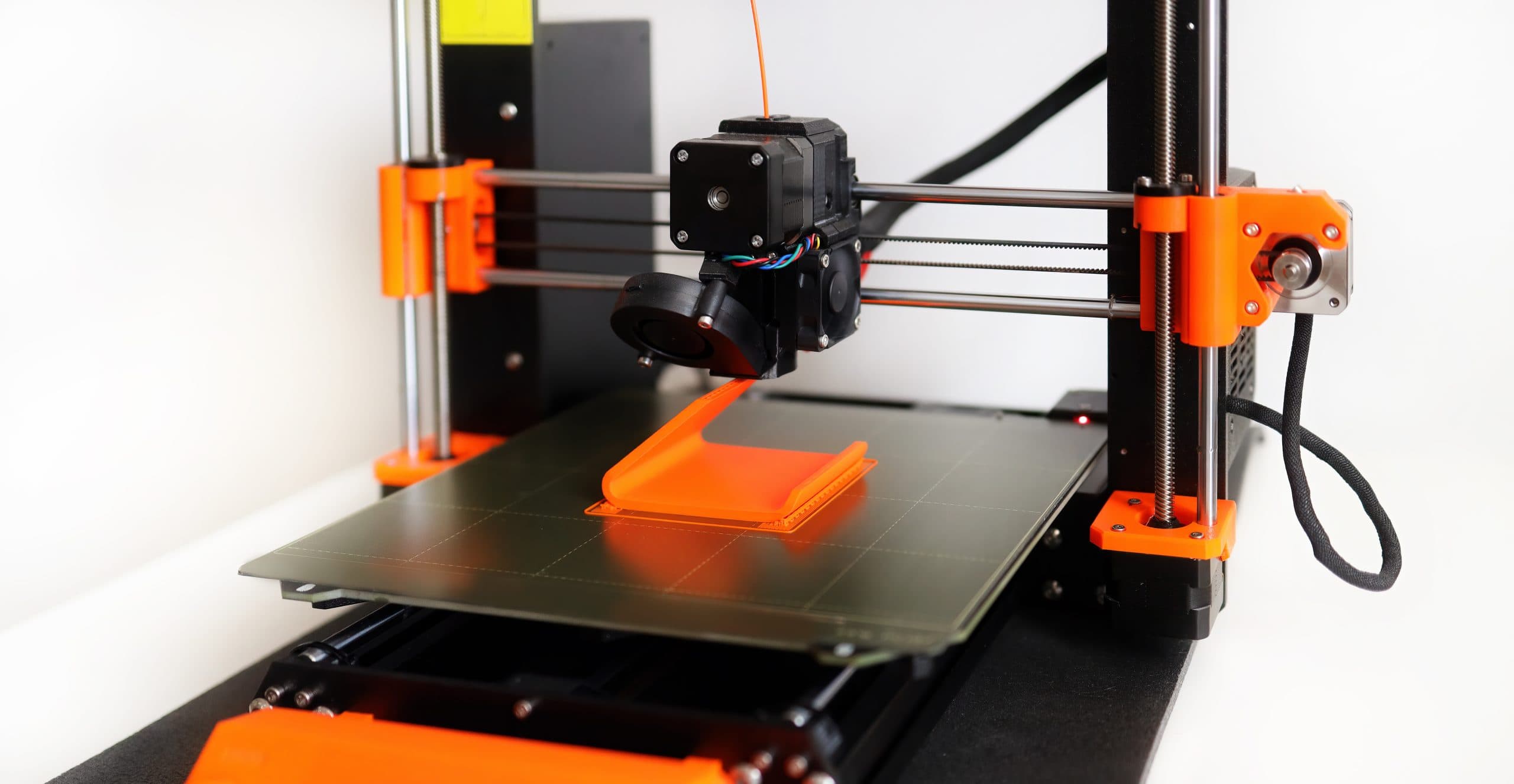 3d,Printer,In,Operation,With,Orange,Filament,On,A,White